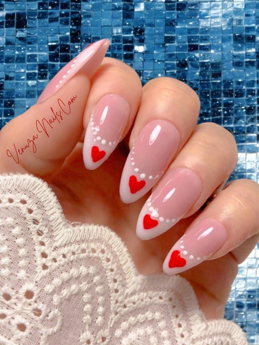 Faux ongles press-on rose nude à french blanche, nail art cœurs rouges et perles blanches, modèle romantique Venuza Nails.