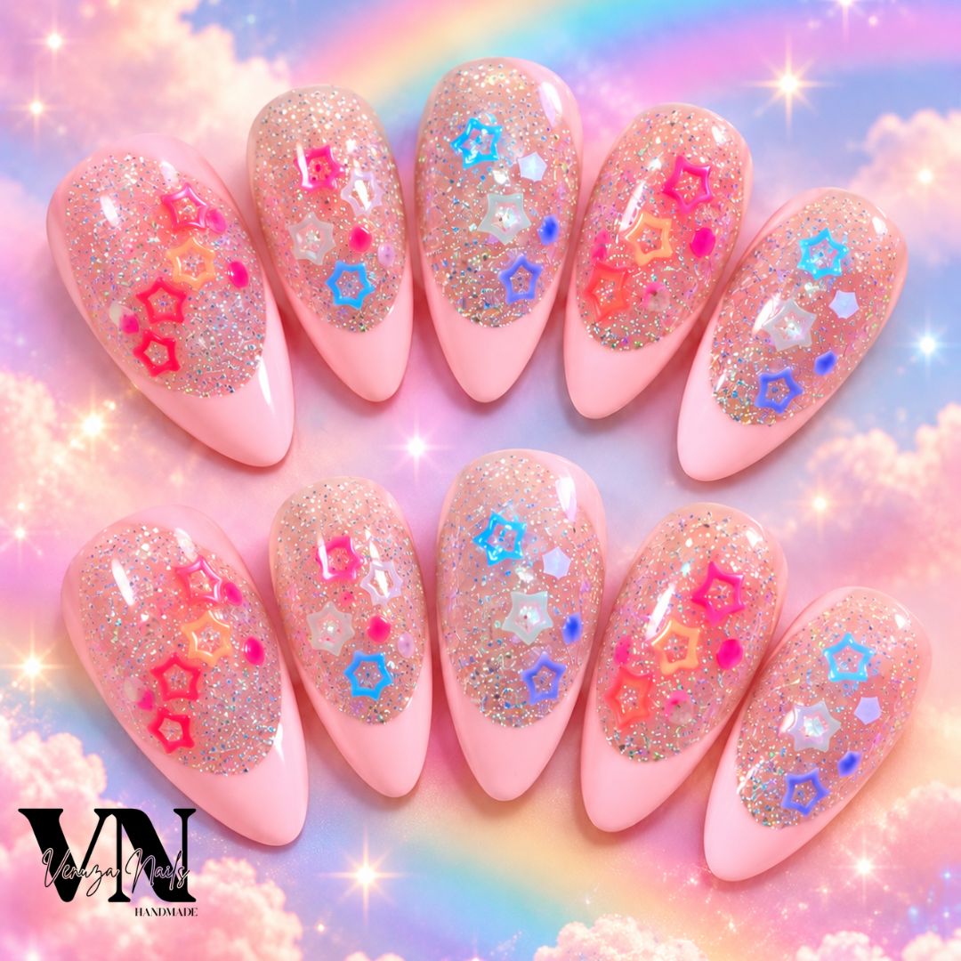 Manucure press-on en forme amande avec French rose pâle, paillettes holographiques et charms étoiles colorés sur une main.