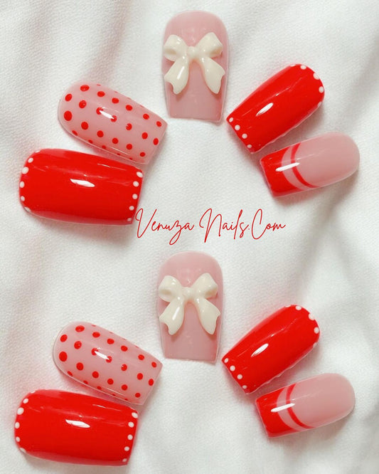 Ensemble de press-on nails rouges et nude décorés de pois blancs, de french rouges et d’un nœud 3D blanc, présenté avec un fond lumineux et festif