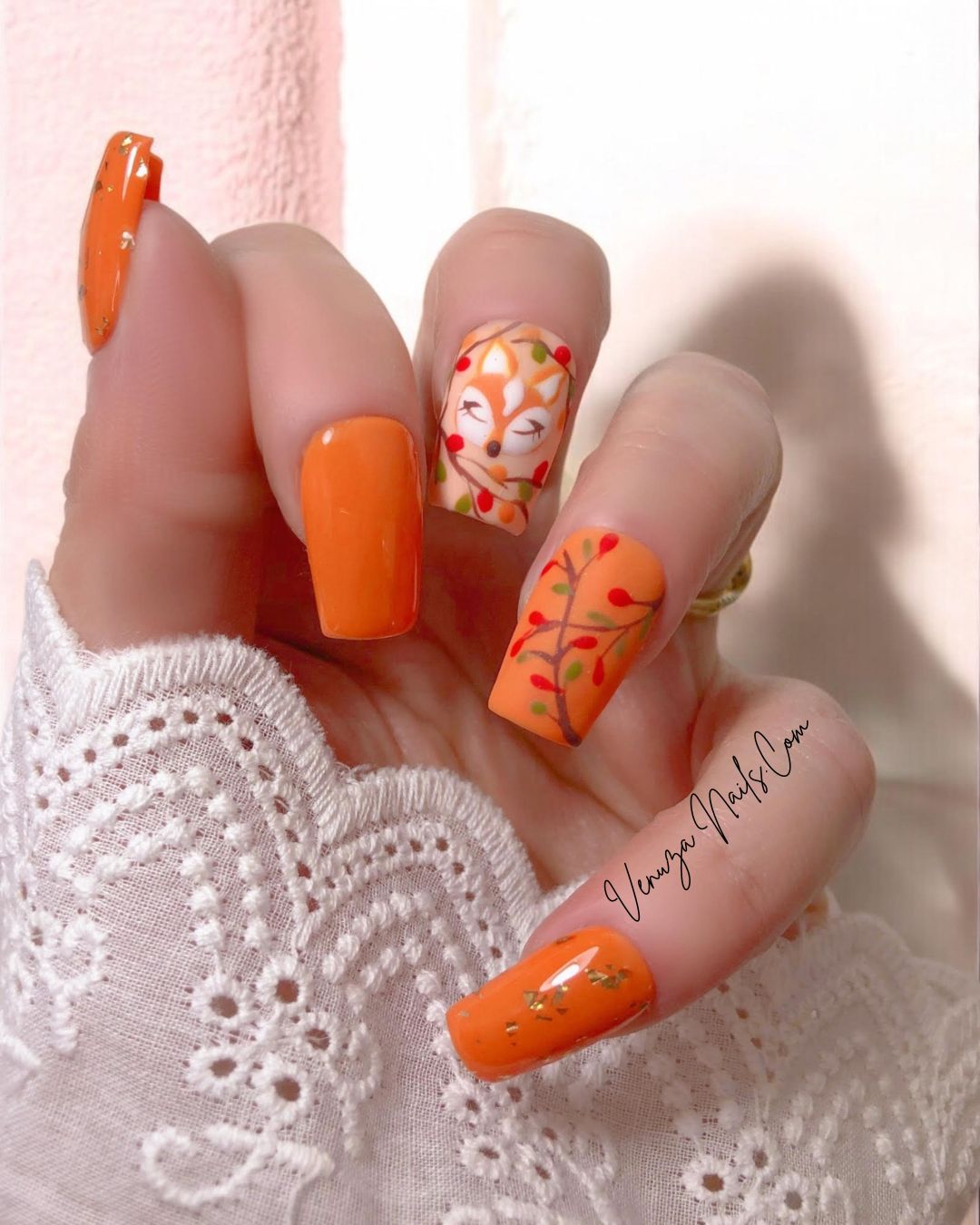Modèle « Rêve d’Automne » de Venuza Nails porté sur une main féminine : press-on nails orange élégants ornés d’éclats de feuilles d’or, d’un motif de renarde endormie et de branches garnies de baies, pour une manucure automnale poétique et raffinée.