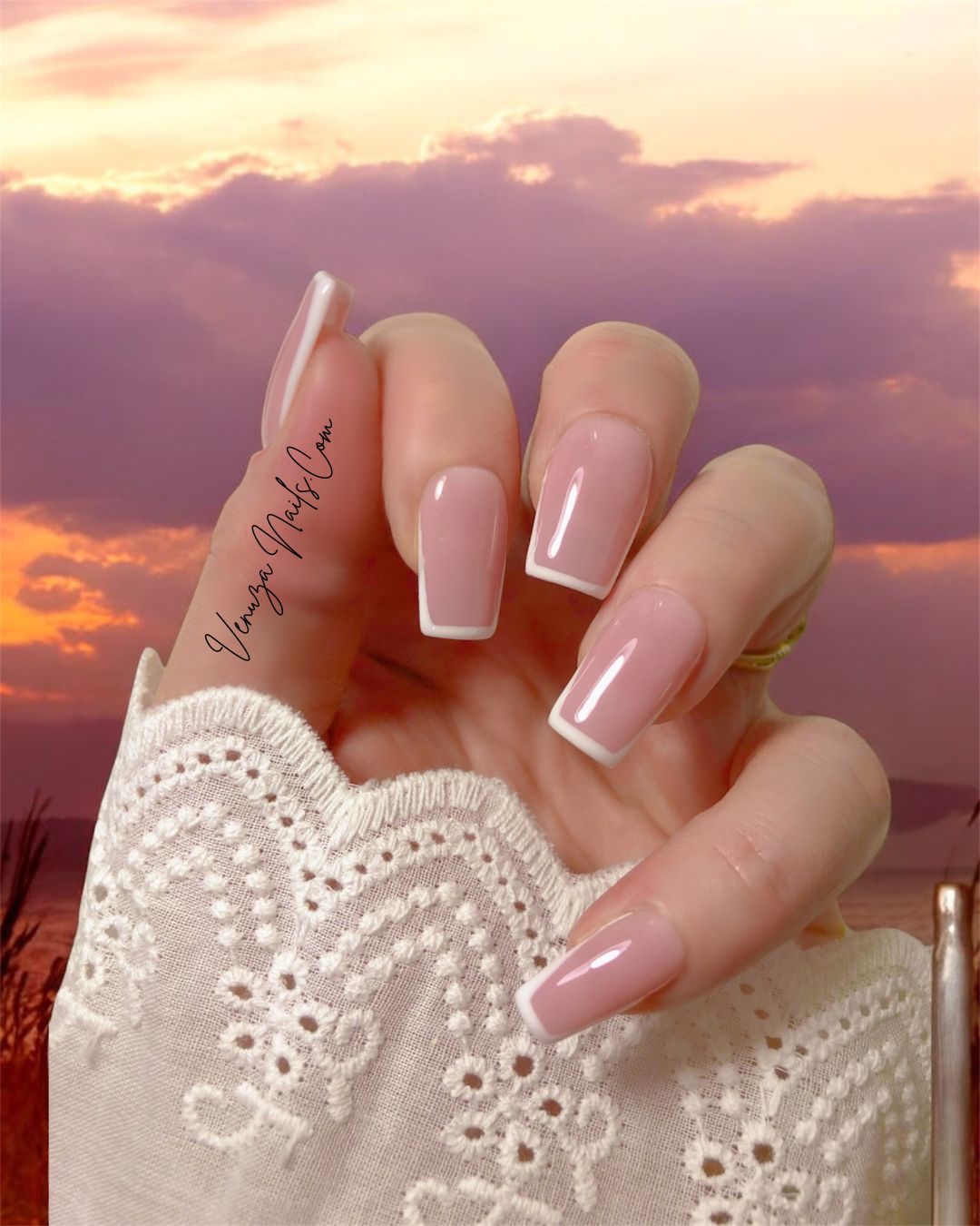 main de femme portant un set de dix ongles sur fond de coucher de soleil los angeles vibes, french contour en carré medium, french manucure moderne et tres chic