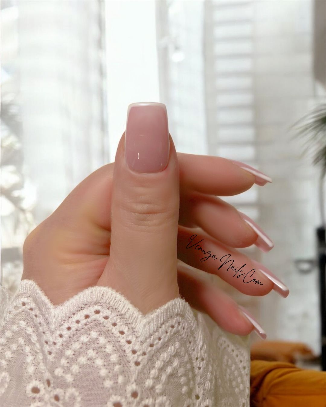 main de femme portant un set de dix ongles sur fond blanc canapé avec couverture caramel, french contour en carré medium, french manucure moderne et tres chic