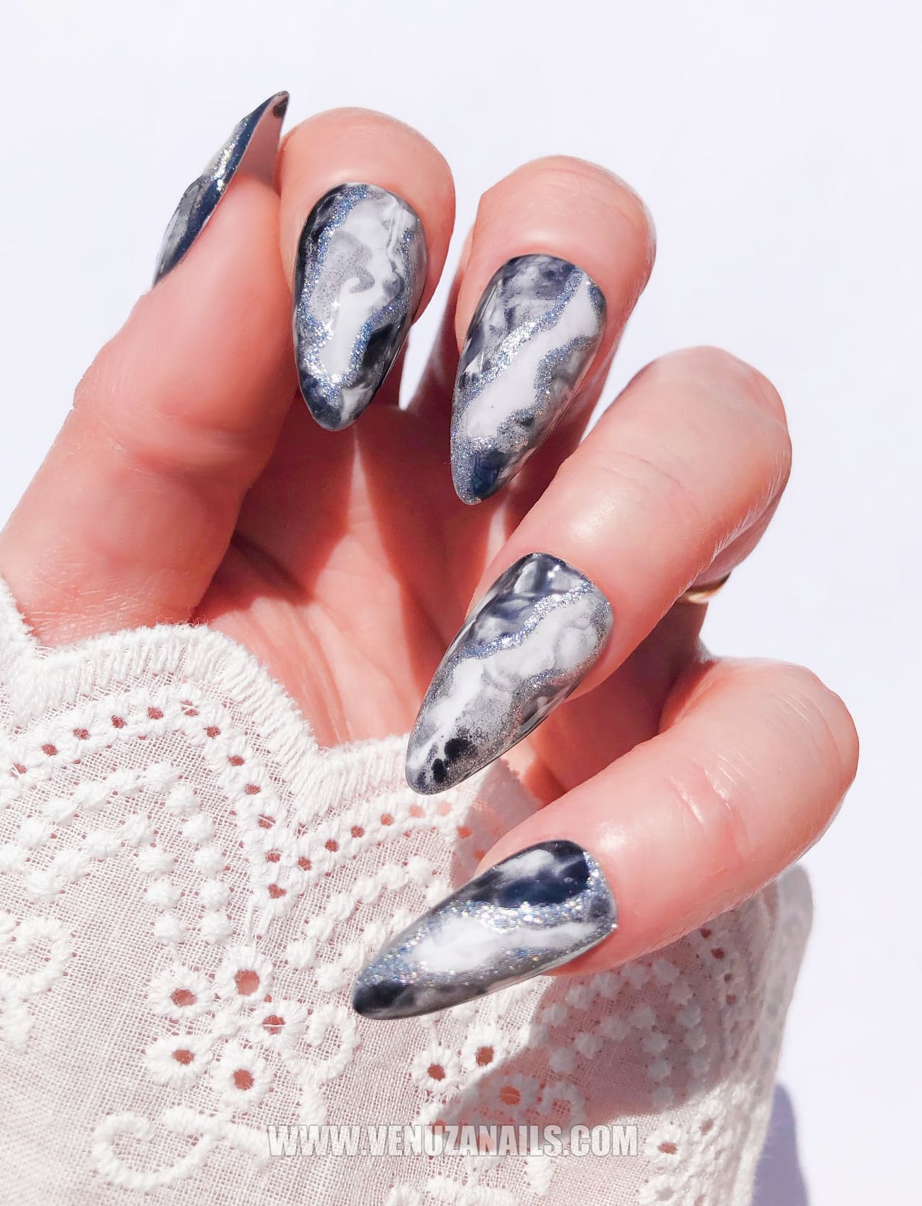 Mains portant des press-on nails marbrés noirs et argentés “Mystic Black”, finition brillante avec des détails métallisés, design élégant et sophistiqué, idéal pour un look chic et audacieux.