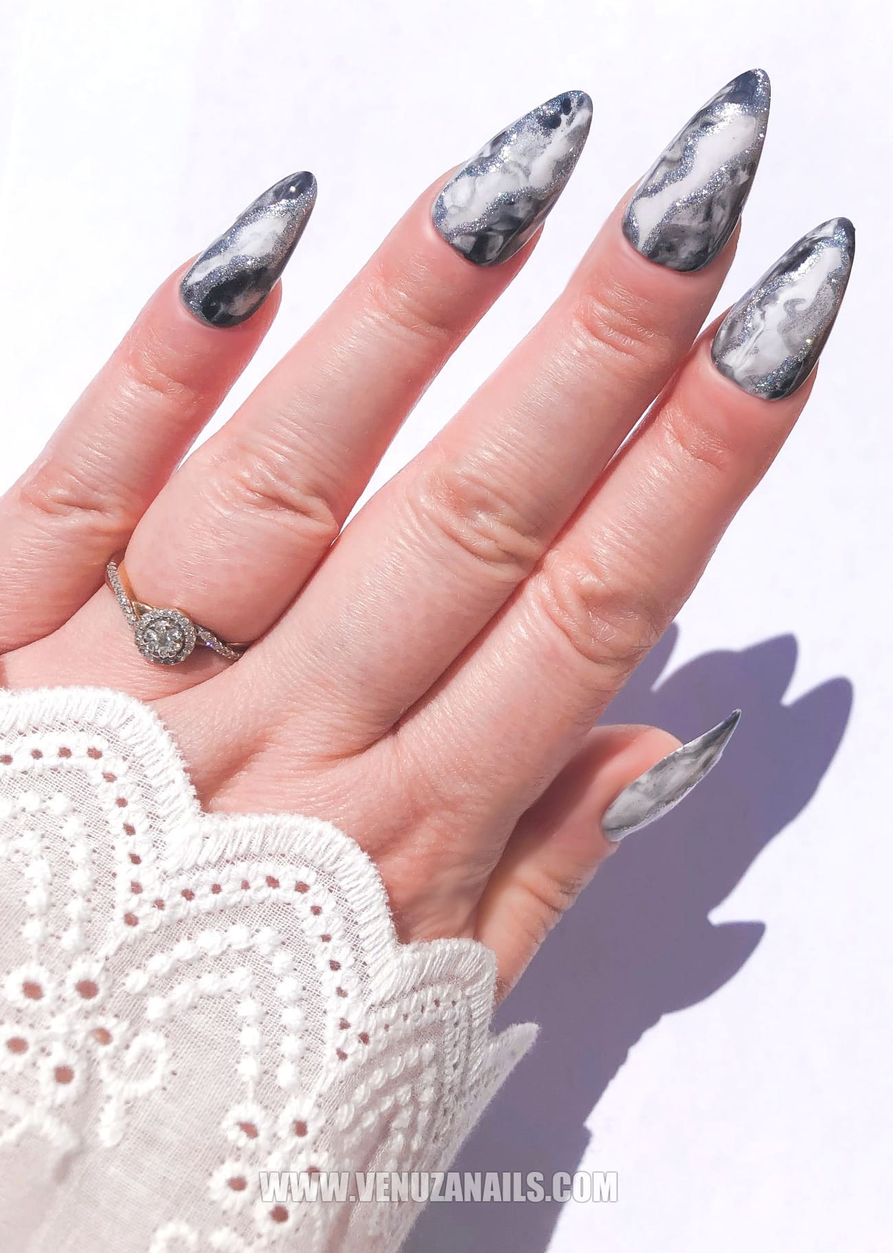 Mains portant des press-on nails marbrés noirs et argentés “Mystic Black”, finition brillante avec des détails métallisés, design élégant et sophistiqué, idéal pour un look chic et audacieux.