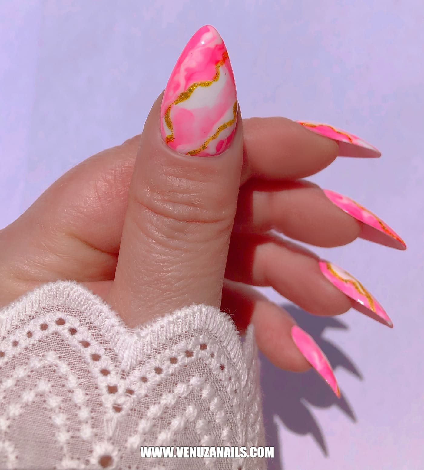 main montrant les faux ongles faits main, marbrés, rose, or, blanc, avec petite manchette en dentelle blanche.