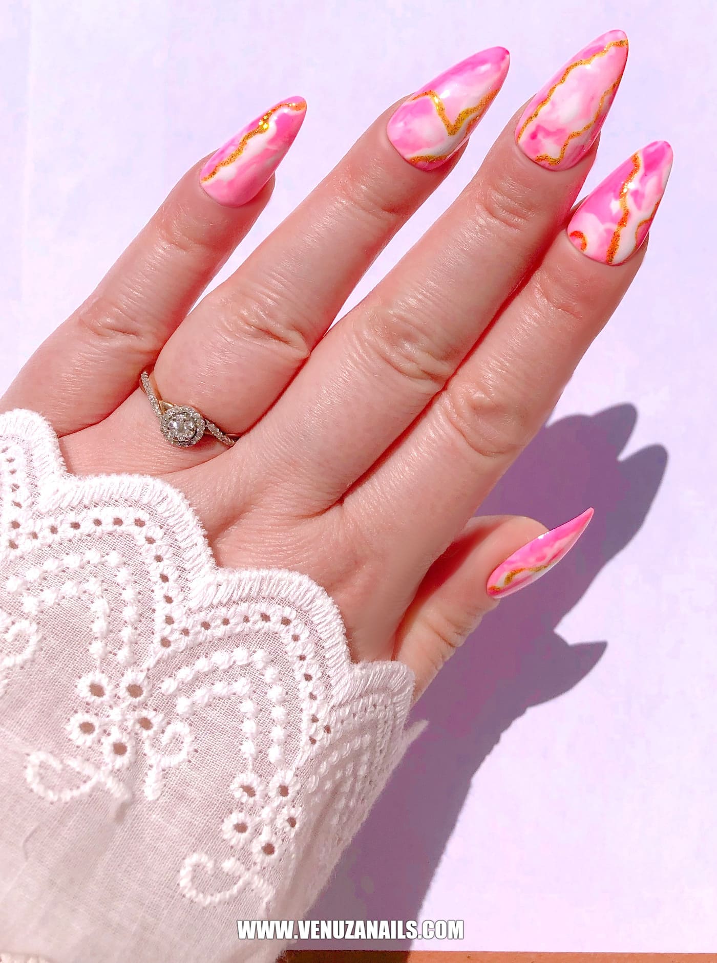 main montrant les faux ongles faits main, marbrés, rose, or, blanc, avec petite manchette en dentelle blanche.