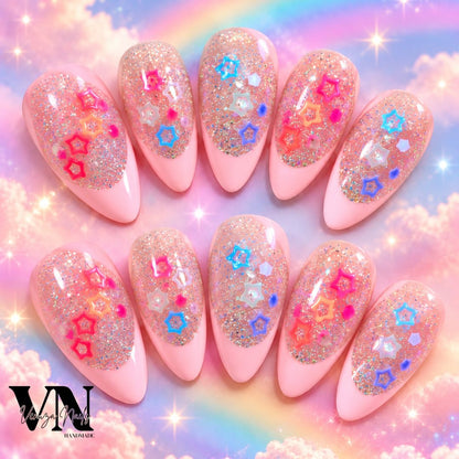 Manucure press-on en forme amande avec French rose pâle, paillettes holographiques et charms étoiles colorés sur une main.