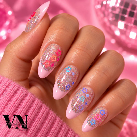 Manucure press-on en forme amande avec French rose pâle, paillettes holographiques et charms étoiles colorés sur une main.