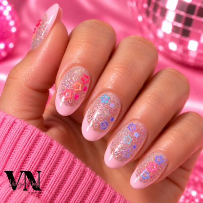 Manucure press-on en forme ovale  avec French rose pâle, paillettes holographiques et charms étoiles colorés sur une main.