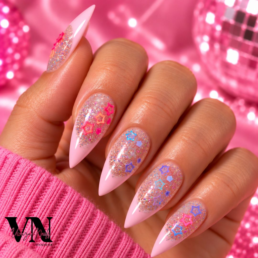 Manucure press-on en forme stiletto avec French rose pâle, paillettes holographiques et charms étoiles colorés sur une main.