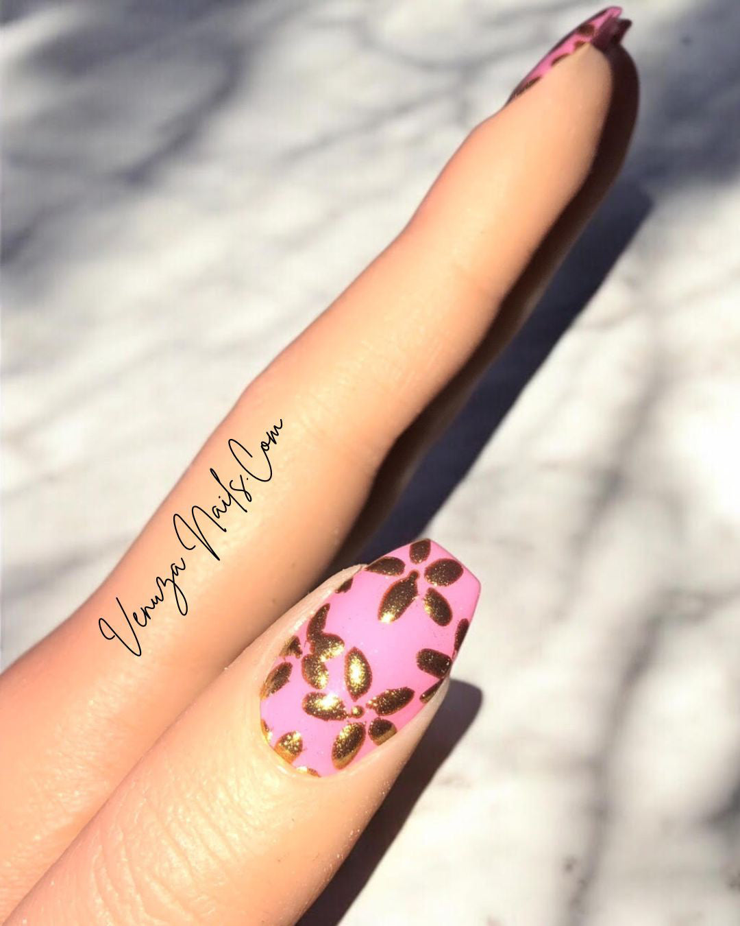 Main de femme présentant de beaux press on nails rose avec de fines fleurs dorées créations signées Venuza Nails