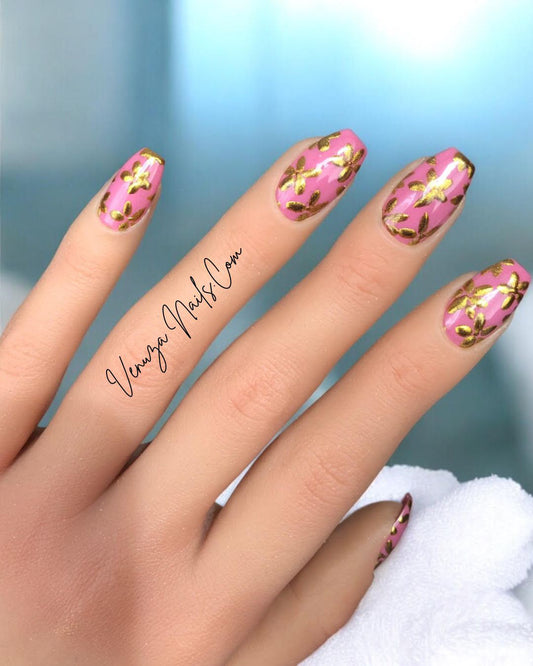 Main de femme présentant de beaux press on nails rose avec de fines fleurs dorées créations signées Venuza Nails