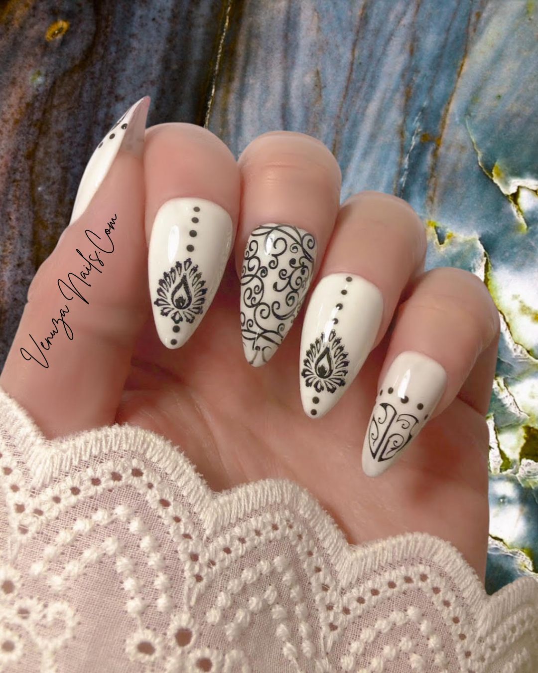 main féminine portant un set de press on nails blancs aux motifs noirs de style baroque, avec arabesques , petits points délicats et volutes, peints à la main par Venuza Nails