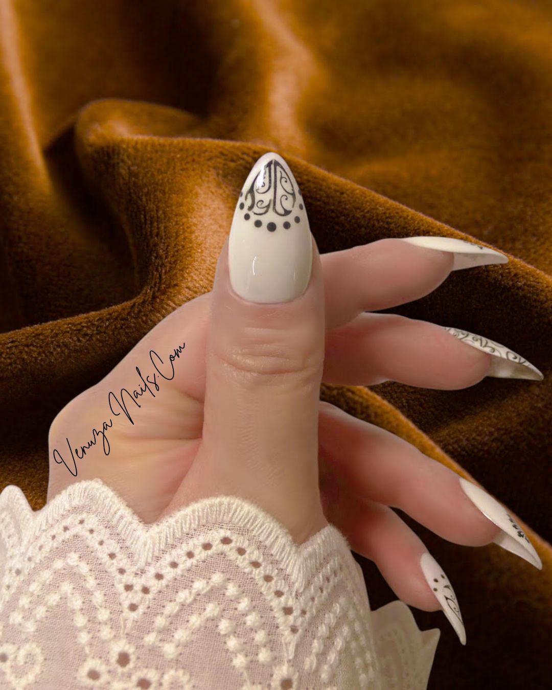 main féminine portant un set de press on nails blancs aux motifs noirs de style baroque, avec arabesques , petits points délicats et volutes, peints à la main par Venuza Nails