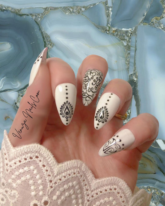 main féminine portant un set de press on nails blancs aux motifs noirs de style baroque, avec arabesques , petits points délicats et volutes, peints à la main par Venuza Nails