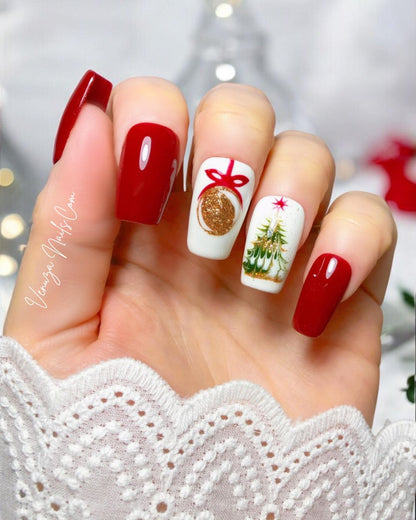 Main portant des press-on nails rouges et blancs au style Noël. Deux ongles sont rouges brillants, un ongle blanc avec une boule dorée dessinée avec un ruban rouge, et un autre ongle blanc décoré d’un petit sapin de Noël doré et vert. Les capsules sont longues et brillantes, avec une ambiance festive et élégante.