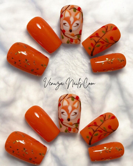 Faux ongles press-on « Rêve d’Automne » de Venuza Nails, dans des teintes orangées chaleureuses décorées de feuilles d’or, d’un motif de renarde endormie entourée de baies colorées, présentés sur un fond blanc duveteux rappelant la douceur de l’automne.