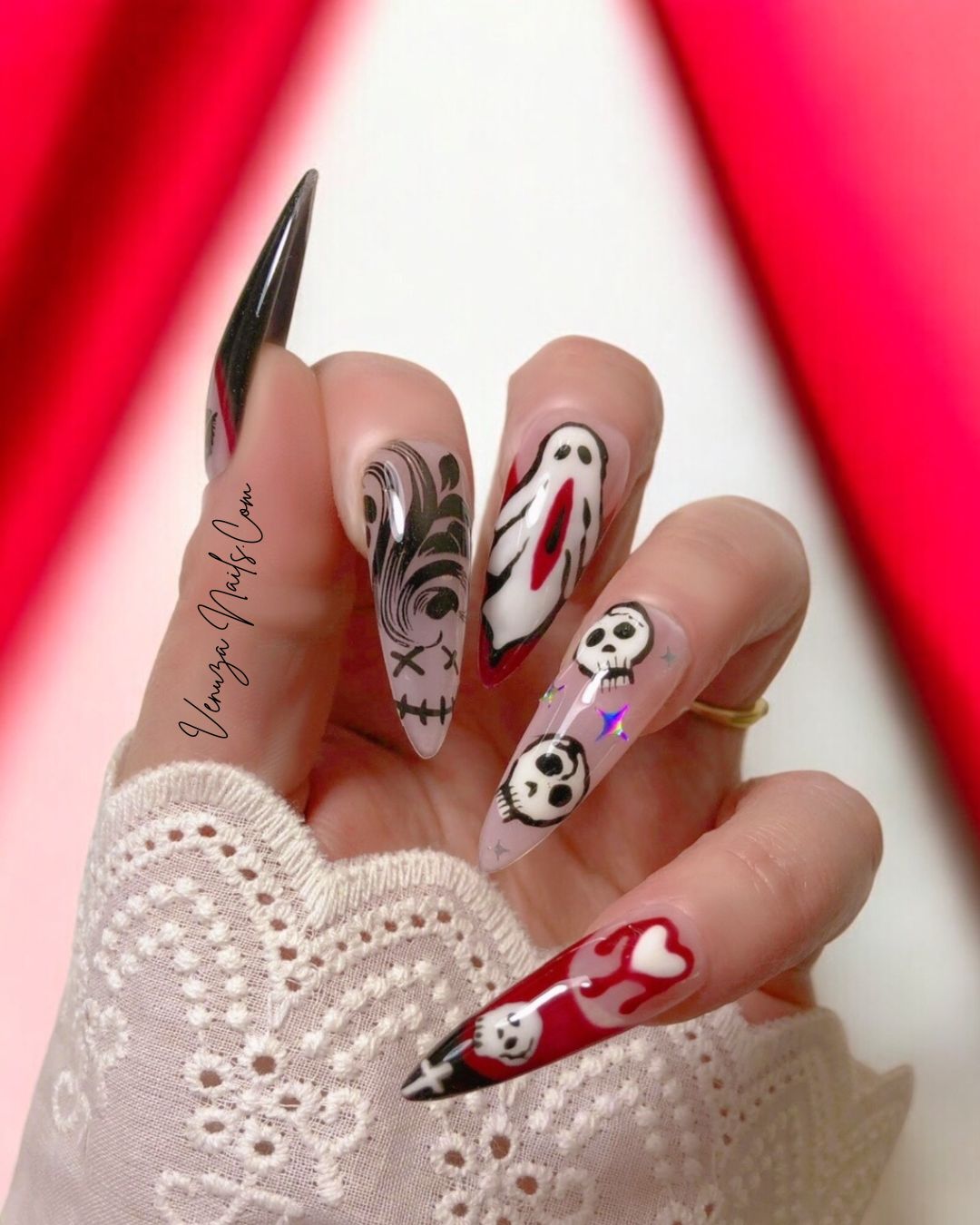main de femme portant un set de press on nails pour halloween, design de fantomes hurlants, de cranes sur fond nude avec étoiles holographiques, french rouges et noires avec coeurs sanglants, et bouches sexy et noires sur une french noire.