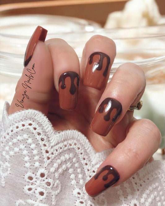 Press-on nails marron chocolat au design gouttes fondantes portés sur main de femme, pour un rendu élégant, sophistiqué et ultra gourmand, idéal pour la saison automnale.