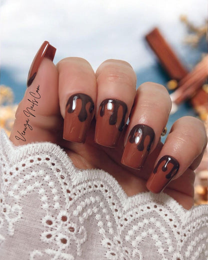 Press-on nails marron chocolat au design gouttes fondantes portés sur main de femme, pour un rendu élégant, sophistiqué et ultra gourmand, idéal pour la saison automnale.