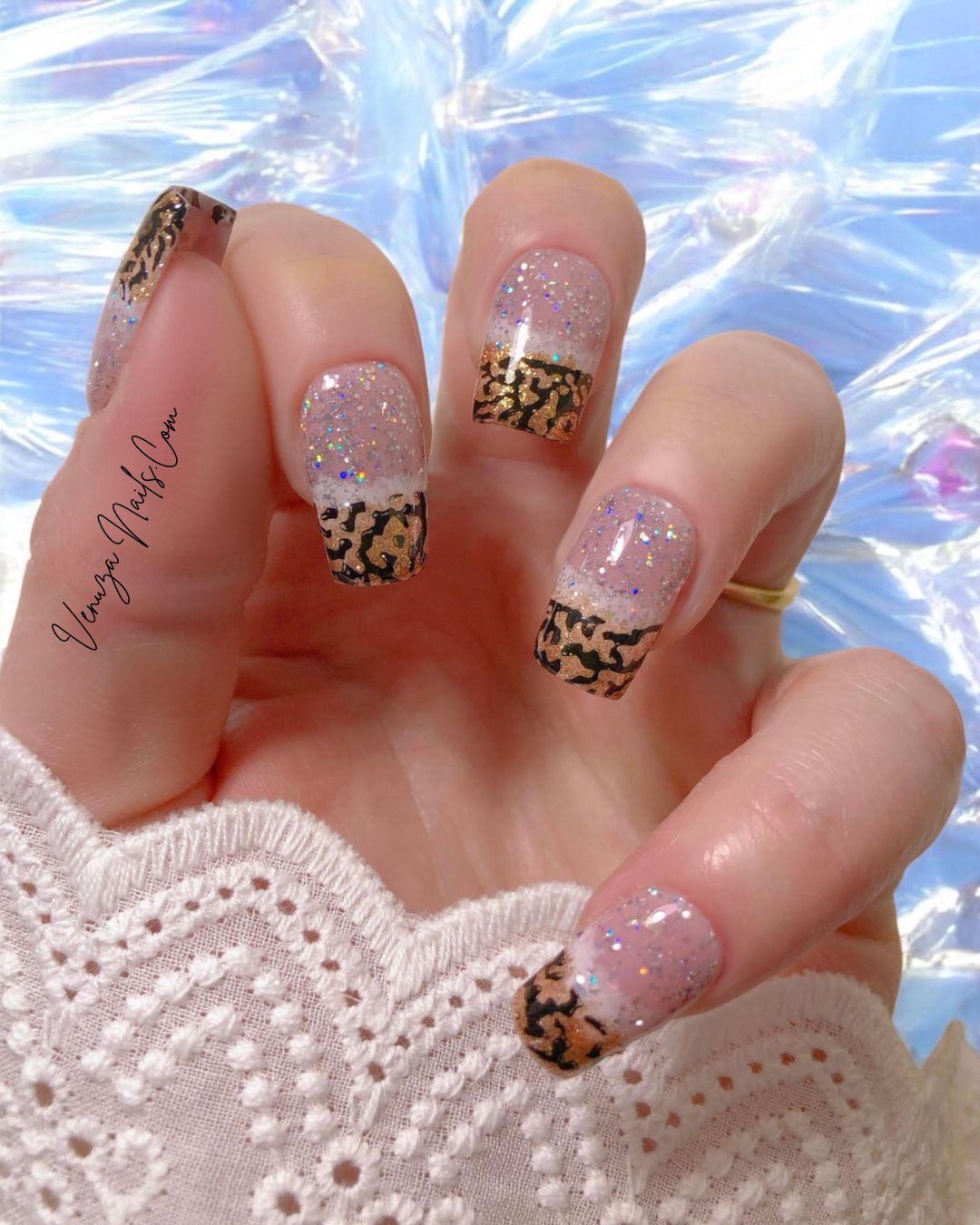 Press-on nails glamour pour Noël – ongles nude et blanc avec paillettes dorées et motif animalier chic.