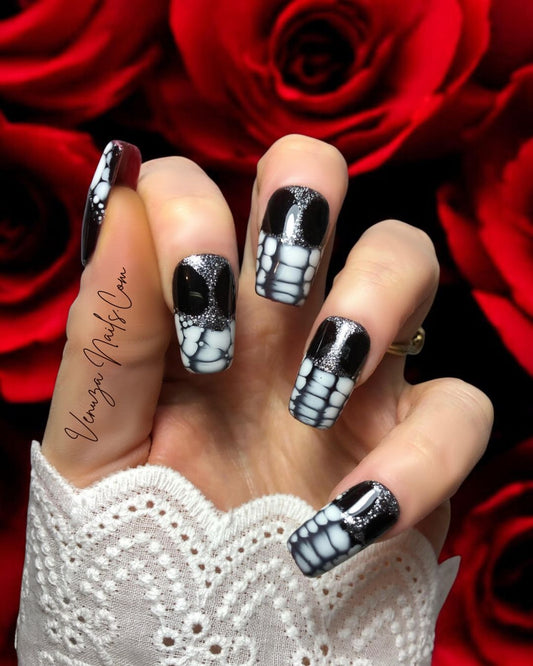 Main féminine portant des press-on nails longs, brillants, noirs avec reflets argentés et effet blooming blanc sur les extrémités, sur fond de roses rouges