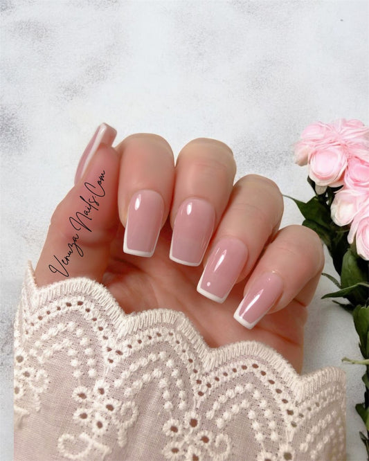 main de femme portant un set de dix ongles sur fond blanc avec bouquet de fleurs roses, french contour en carré medium, french manucure moderne et tres chic