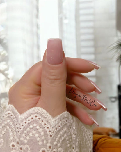 main de femme portant un set de dix ongles sur fond blanc canapé avec couverture caramel, french contour en carré medium, french manucure moderne et tres chic
