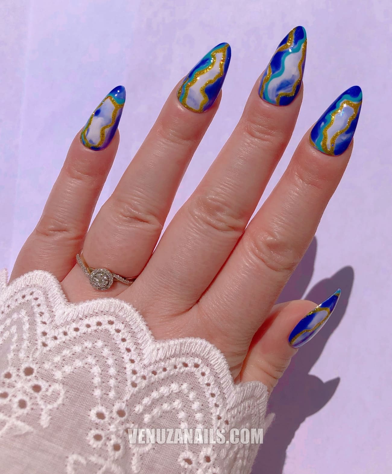 (main avec ongles marbrés bleu, blanc et or) :
alt="Press-on nails marbrés bleu, blanc et or – faux ongles en forme amande de la marque Venuza Nails"