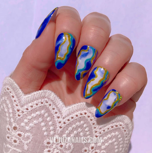 (main avec ongles marbrés bleu, blanc et or) :
alt="Press-on nails marbrés bleu, blanc et or – faux ongles en forme amande de la marque Venuza Nails"