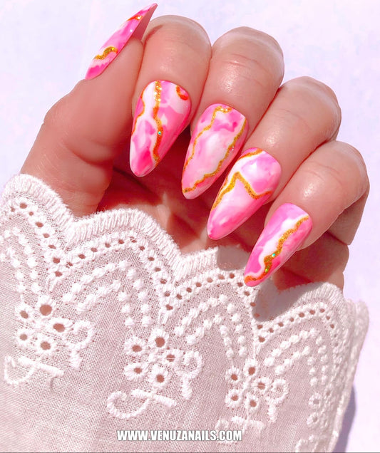 main montrant les faux ongles faits main, marbrés, rose, or, blanc, avec petite manchette en dentelle blanche.