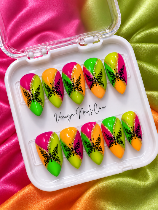 Faux ongles press-on Tropica aux couleurs néon fuchsia, vert citron et orange, décorés de papillons noirs et de lignes diagonales à paillettes dorées, création artisanale Venuza Nails. 